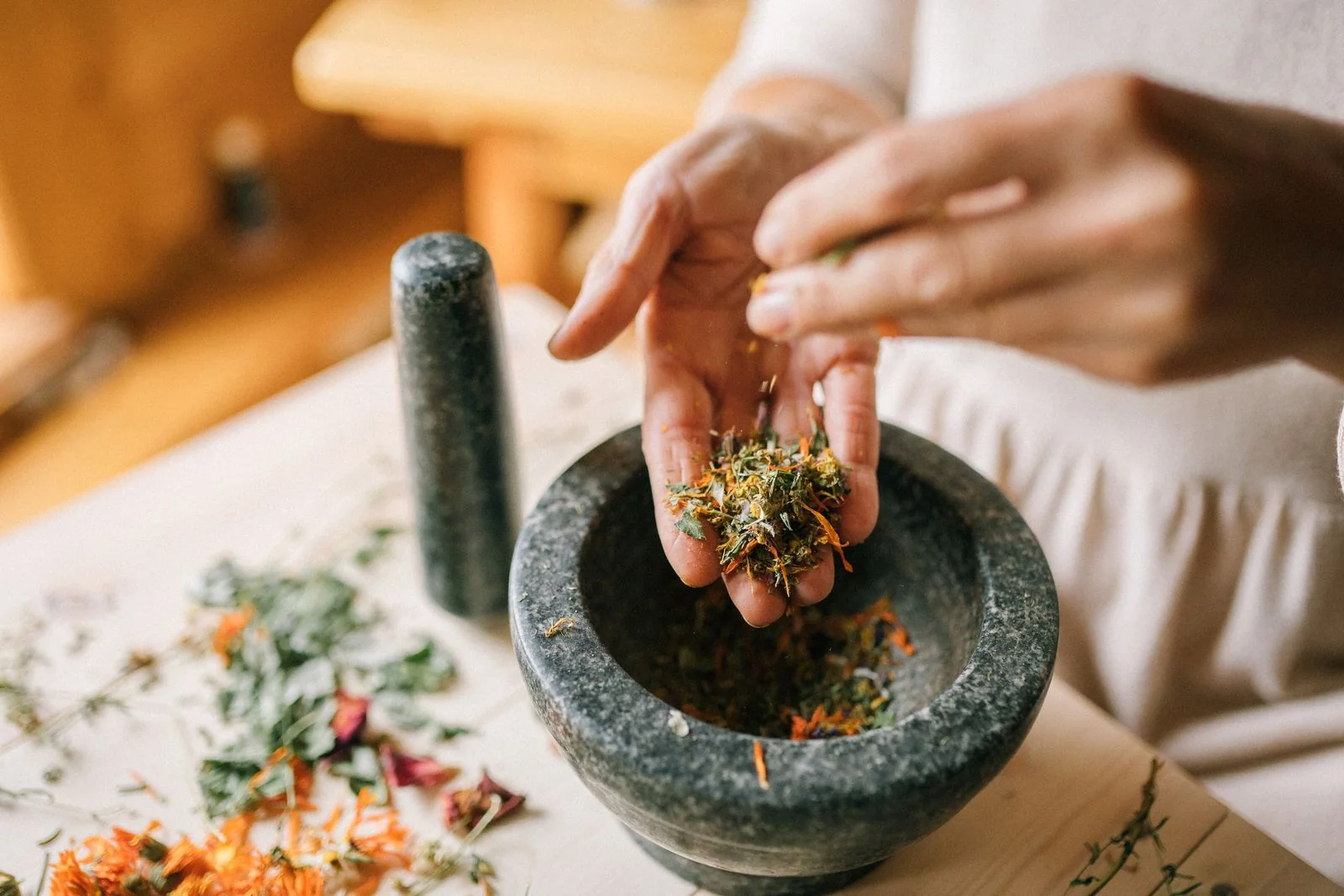 Hands measuring dried herbs into a stone mortar